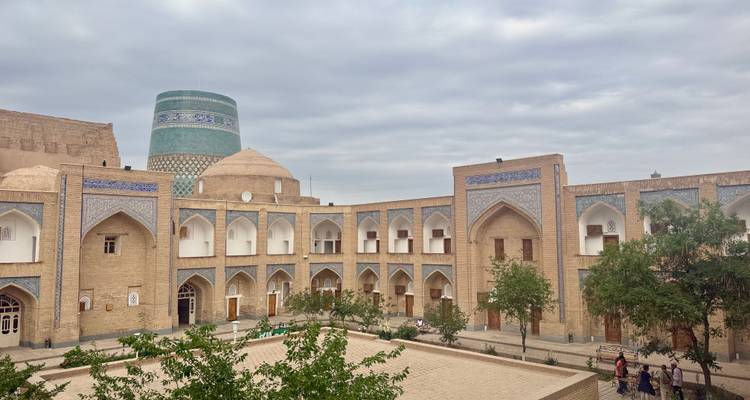 Courtyard view of Khiva's mud-brick architecture with the turquoise Kalta Minor minaret rising behind.
