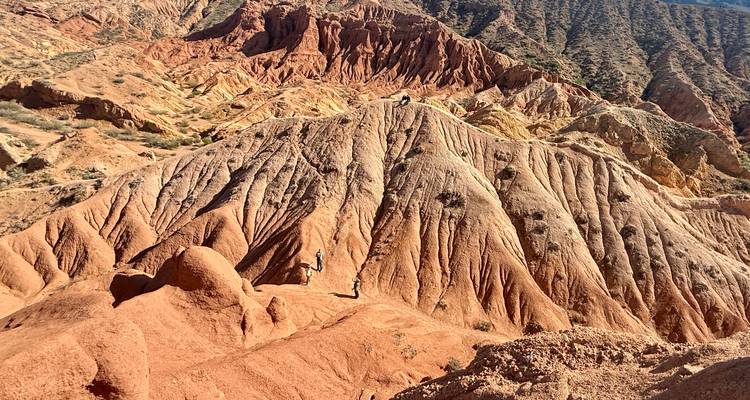 Vivid red and orange sandstone ridges and gullies of Kyrgyzstan's Fairytale Canyon under bright sun.
