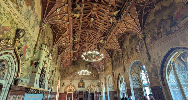Weelderig grote zaal met ingewikkeld uitgesneden houten plafond, kroonluchters en geschilderde muurschilderingen.