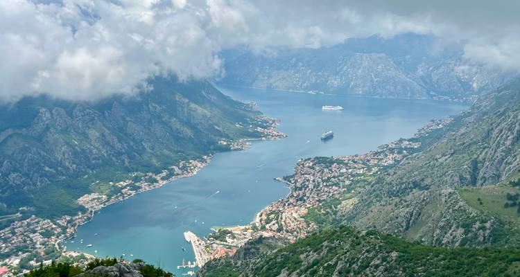 Une vue aérienne panoramique de la baie de Kotor serpente entre des montagnes spectaculaires sous des nuages qui dérivent.