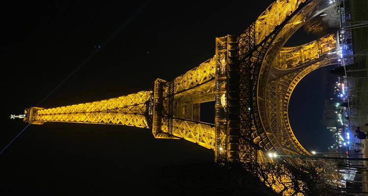 La Tour Eiffel brillant d'or contre le ciel nocturne noir, vue depuis sa base.