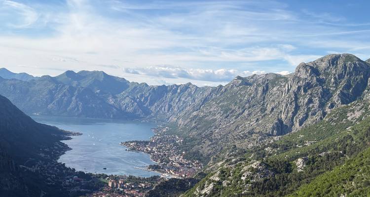 Vista panorámica de la Bahía de Kotor con dramáticas montañas de piedra caliza y un pueblito costero abajo.