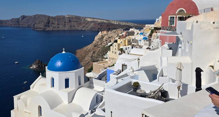 Scène classique de Santorin avec une église aux dômes bleus et des maisons cycladiques blanches perchées au-dessus de la caldeira d'un bleu profond.