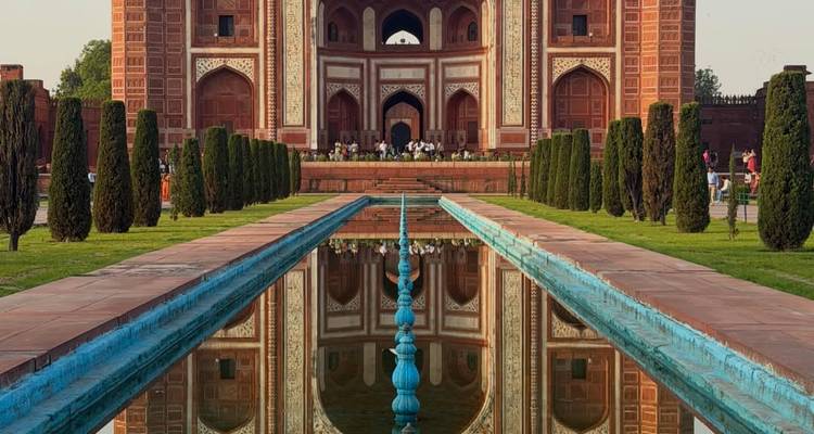 Reflejo simétrico de la gran puerta de arenisca roja del complejo del Taj Mahal en un largo estanque al amanecer.