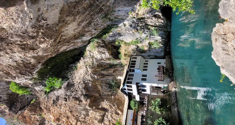Monasterio White Dervish escondido bajo un acantilado imponente junto a las aguas de manantial color turquesa en Blagaj Tekke