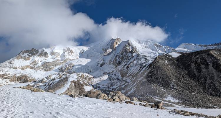 Imposante face himalayenne couverte de neige s'élevant dans un ciel bleu profond et limpide avec des nuages à la dérive.