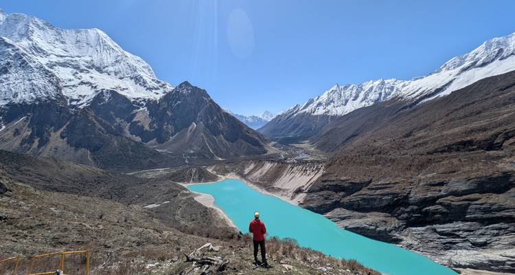 Randonneur surplombant un lac glaciaire d'un bleu turquoise frappant, situé au milieu de chaînes himalayennes spectaculaires aux sommets enneigés.