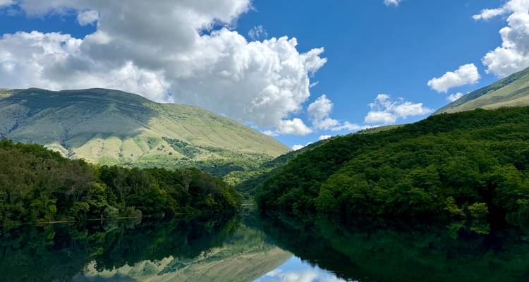 Lac aux reflets miroir reflétant des collines verdoyantes luxuriantes et des nuages gonflés sous un ciel bleu.