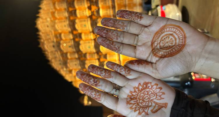 Zwei Hände mit frischen Henna-Mustern, die gegen die beleuchtete Fassade des Hawa Mahal in der Nacht gehalten werden.