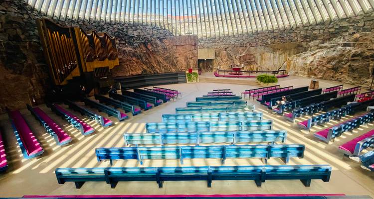 Intérieur spectaculaire d'une église creusée dans le roc avec des fentes de lumière zénithale et des bancs de couleur.