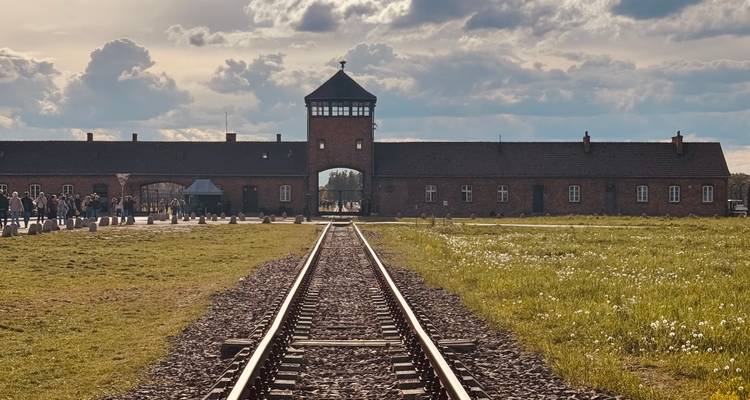 Las icónicas vías de tren que llevan a la puerta de entrada de ladrillo de Auschwitz-Birkenau bajo un cielo dramático.