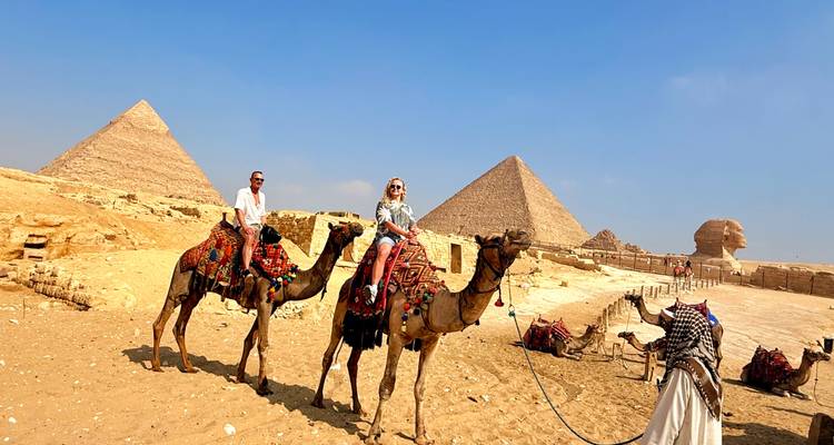Turistas montando camellos frente a las Pirámides y la Esfinge en el desierto