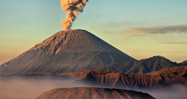 Volcan actif émettant un épais panache de cendres au-dessus d'un cône côtelé au lever du soleil avec une caldeira brumeuse en dessous