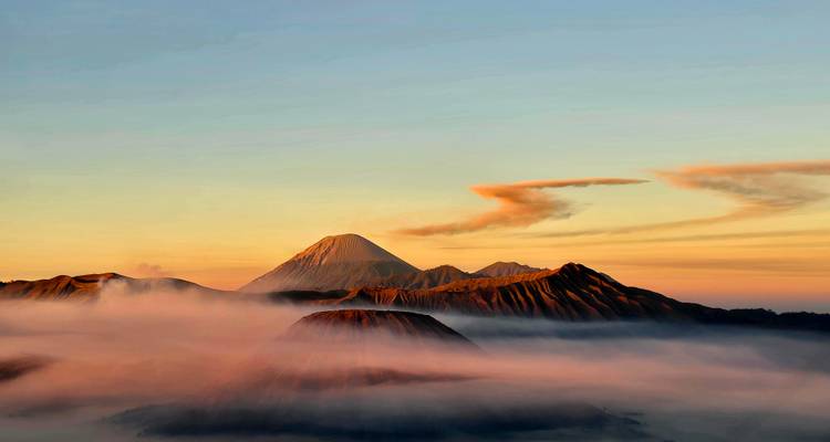 Mer de nuages illuminée par la lumière de l'aube entourant les pics volcaniques en couches du massif de Bromo Tengger