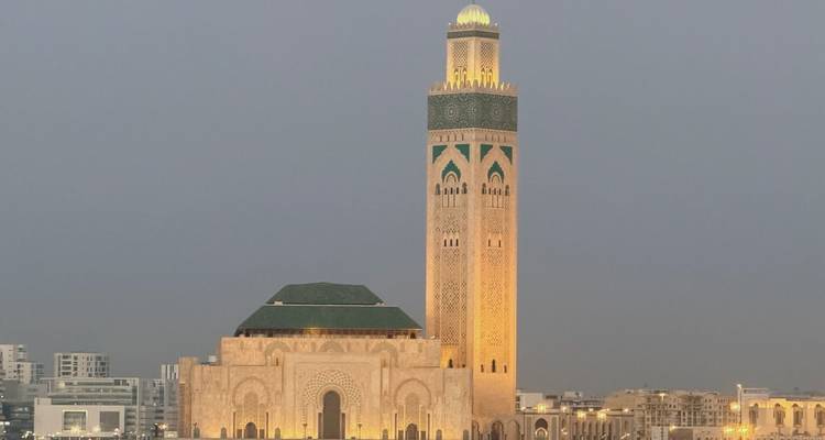 Mezquita Hassan II iluminada con luz cálida contra un cielo gris crepuscular que domina Casablanca
