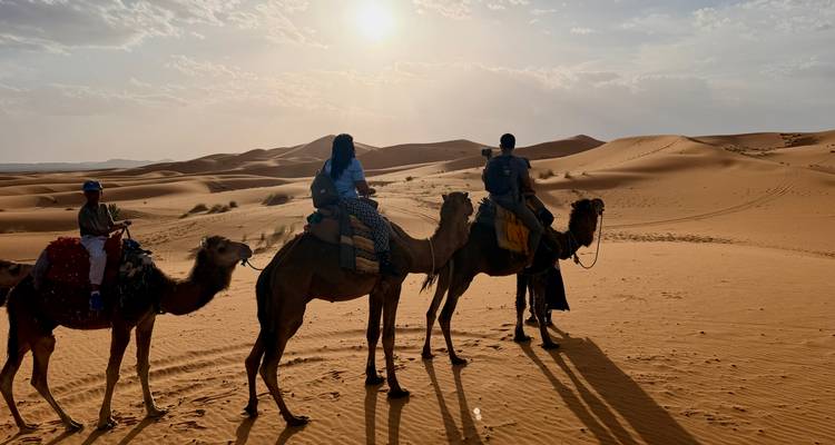 Jinetes silueteados en camellos caminando por las dunas ondulantes del Sahara bajo el sol poniente