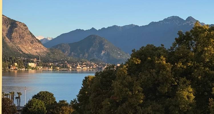 Lac serein bordé de collines boisées et de pics alpins lointains sous un ciel bleu dégagé.