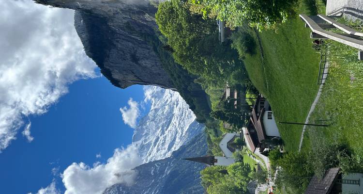 Village alpin pittoresque avec église à clocher sous des falaises montagneuses enneigées et un ciel bleu