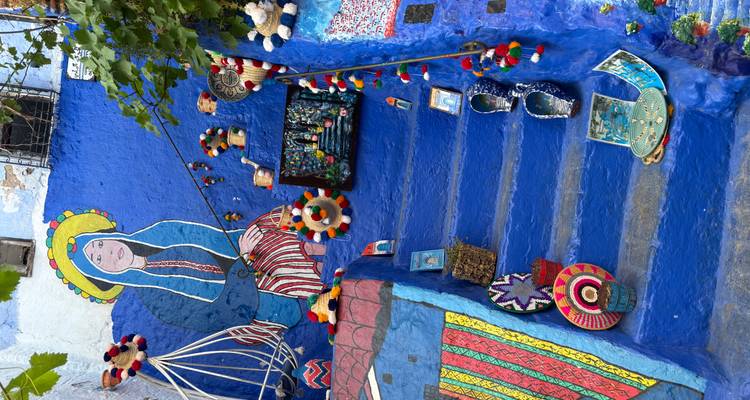 Escalera pintada de un azul brillante en Chefchaouen decorada con arte folclórico, textiles coloridos y artesanías hechas a mano.