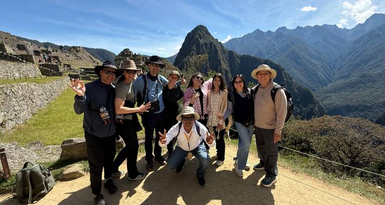 Groupe de touristes célébrant aux terrasses emblématiques du Machu Picchu avec le pic Huayna Picchu en arrière-plan.