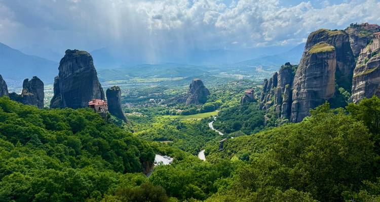 Vue panoramique des piliers rocheux luxuriants de Meteora et des monastères sous un ciel dramatique.