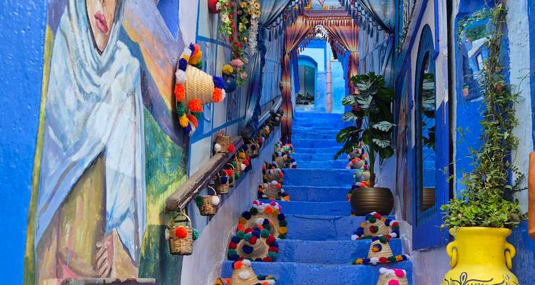Ruelle d'un bleu éclatant à Chefchaouen décorée de chapeaux tissés colorés et de peintures murales menant à des escaliers peints.