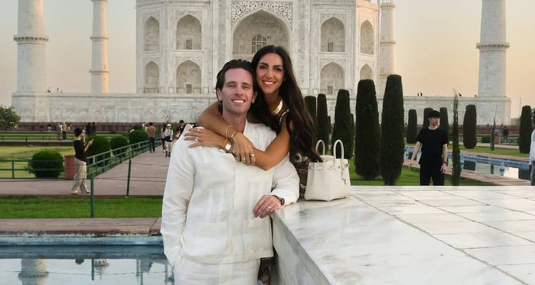 Una pareja sonriente se abraza frente al Taj Mahal al atardecer, con su mármol blanco brillando suavemente.