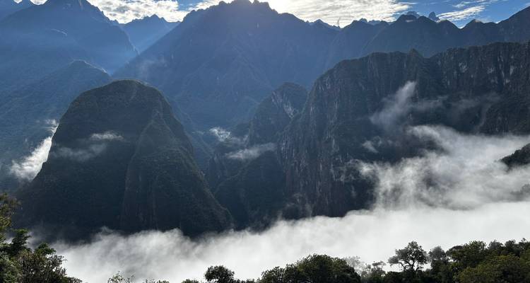 Neblina dramática llenando un profundo cañón con picos verdes escarpados y un cielo retroiluminado sobre los Andes