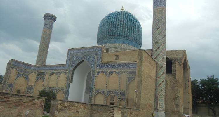 Icónico Mausoleo Gur-e-Amir en Samarcanda con su cúpula de azulejos azules y altos minaretes bajo un cielo tormentoso.