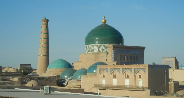 Silueta de Jiva con cúpulas cubiertas de tejas verdes y un esbelt minarete brillando en la luz de la mañana.