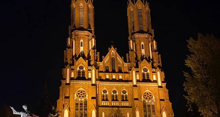 Iglesia de dos torres de ladrillo iluminada dramáticamente contra un cielo nocturno oscuro.