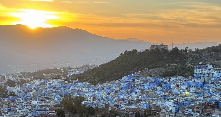 La puesta de sol sobre las Montañas del Rif iluminando la ciudad pintada de azul de Chefchaouen extendiéndose abajo.