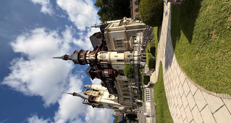Ein prachtvolles Schloss im Neorenaissance-Stil mit Türmen und Balkonen erhebt sich gegen einen strahlenden Himmel und gepflegte Gärten.