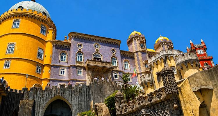 Les tours d'un jaune éclatant et violet du Palais de Pena s'élèvent au-dessus de murs de pierre ornés sous un ciel bleu clair à Sintra.