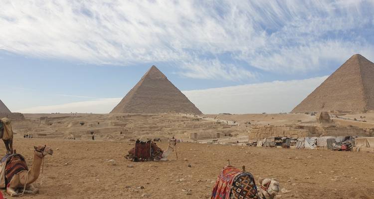 Les pyramides emblématiques de Giza s'élevant du désert de sable avec des chameaux et des couvertures au premier plan sous un ciel strié.