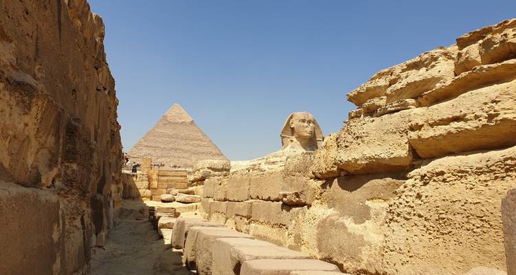 Iconisch uitzicht op de Sphinx omgeven door zandstenen muren met de Piramide van Khafre die in de achtergrond oprijst onder een blauwe lucht.