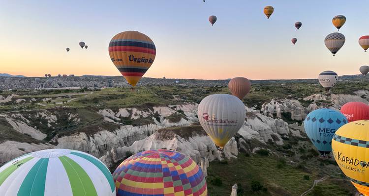Tientallen kleurige heteluchtballonnen zweven bij zonsopgang over de buitenaardse rotsvalleien van Cappadocië.