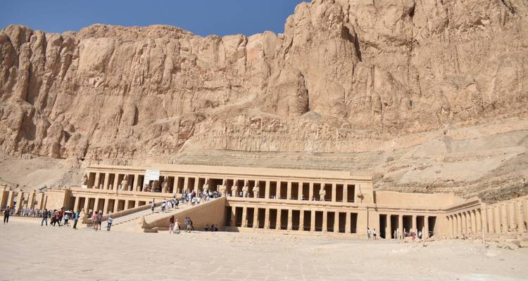 Le Temple en terrasses d'Hatshepsout niché sous de hautes falaises désertiques avec des visiteurs marchant à travers la cour d'honneur.