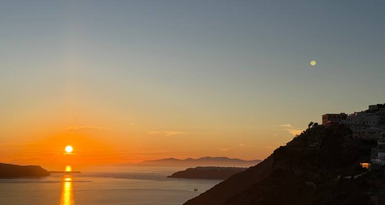 Vibrant sunset over the Santorini caldera with silhouettes of distant islands and calm sea