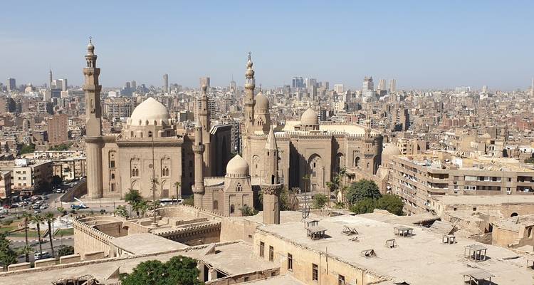 Panoramic view over Cairo featuring historic mosques with domes and minarets set against a sprawling modern skyline.