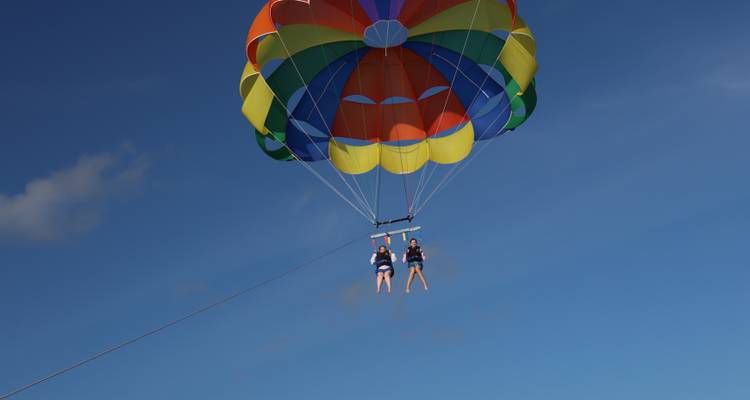 Un parachute ascensionnel coloré soulève deux amateurs de sensations fortes haut dans un ciel bleu dégagé.