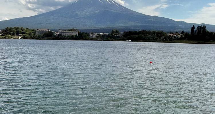 Le Mont Fuji aux pics enneigés se dresse majestueusement au-dessus d'un lac paisible, avec une ville qui s'étend le long de la rive opposée.