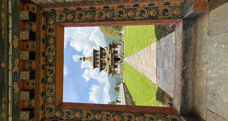 Ein bhutanischer Tempel, umrahmt von einer kunstvoll bemalten Türöffnung, über einen gepflegten Rasen unter blauem Himmel