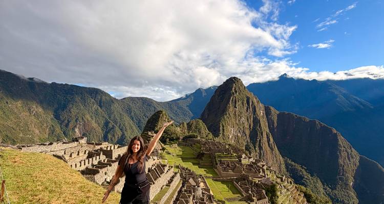 Vista panorámica de las ruinas de Machu Picchu enmarcadas por picos verdes espectaculares bajo un cielo parcialmente nublado.