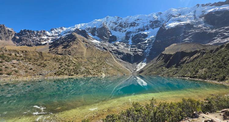 Crystal-clear turquoise Humantay Lake mirroring snow-capped Andean peaks under a deep blue sky.