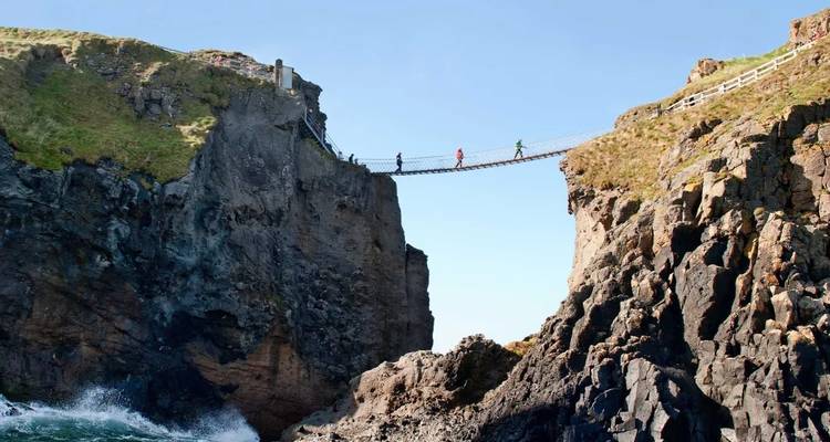 Avonturiers die een smalle hangbrug oversteken hoog tussen rotsachtige zeerotsen