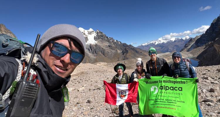 Pequeño grupo de trekking sosteniendo banderas de Perú y de tours con picos nevados de los Andes de fondo