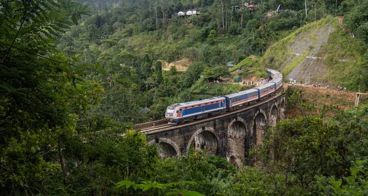 Le train bleu et rouge traverse le pont historique des Neuf Arches au milieu de la jungle verdoyante près d'Ella.