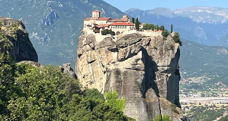 Kloster auf einer dramatischen Felssäule mit grünen Bergen im Hintergrund in Meteora