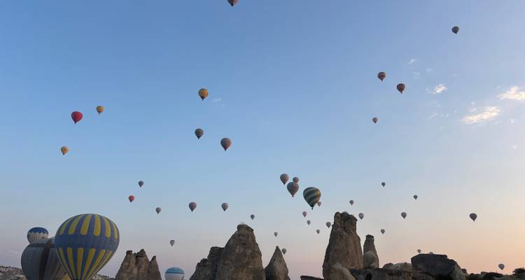Dozens of colorful hot-air balloons rise over Cappadocia’s rock spires at dawn beneath a pastel sky.